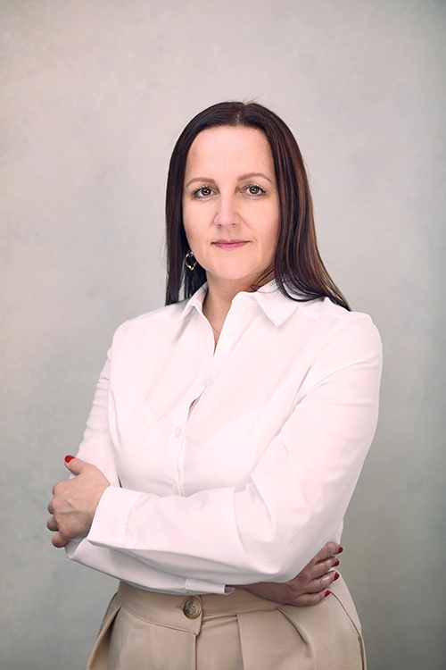 Karolina Maciejczyk in a white shirt and beige trousers, standing with her arms folded