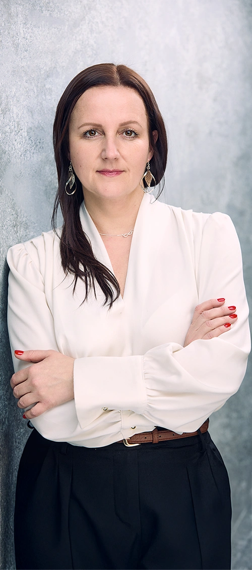 Karolina Maciejczyk is standing and looking straight ahead, her arms are folded, she is wearing a white shirt and black trousers.