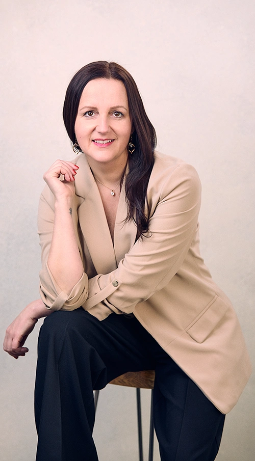 Karolina Maciejczyk sitting on a chair and smiles in a beige jacket and black trousers