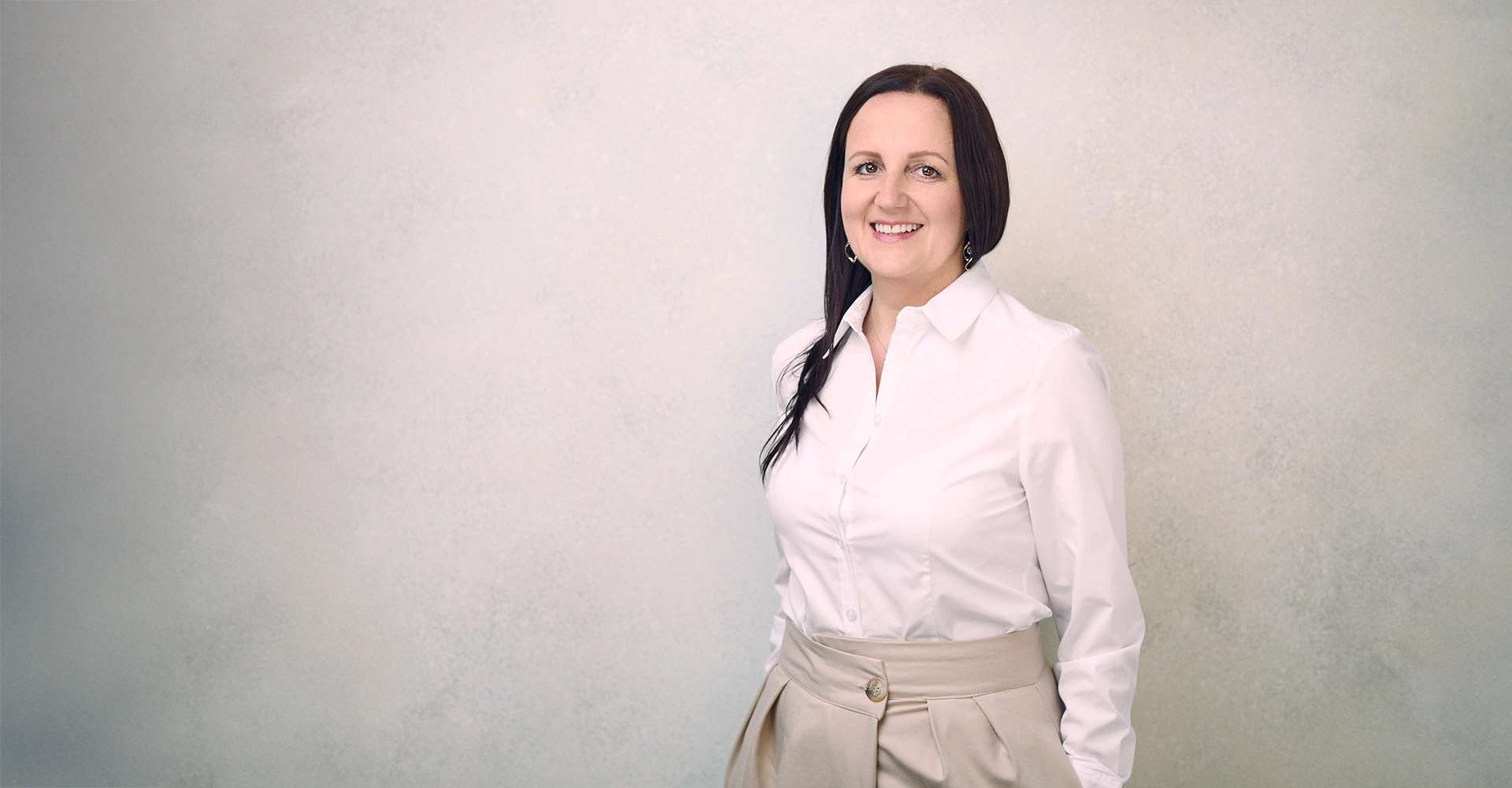 Karolina Maciejczyk stands and smiles, wearing a white shirt and beige trousers.